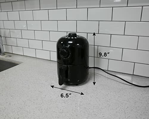 Compact black air fryer on kitchen counter with dimensions labeled.