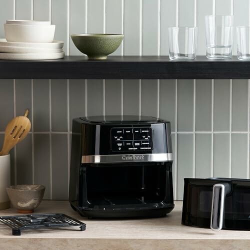 Air fryer on kitchen countertop with dishes and glasses on shelves.